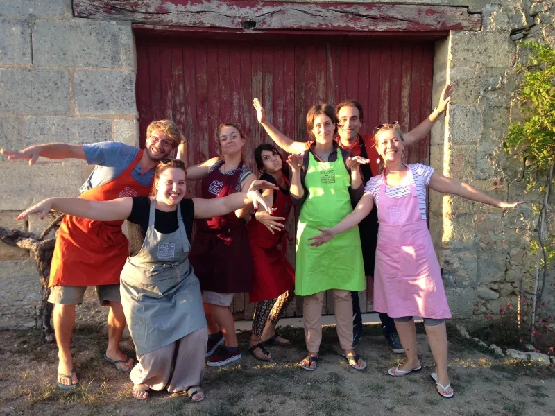 Group of smiling participants posing in front of a red door during an oenological escape game in Bordeaux, with arms raised in celebration and victory.