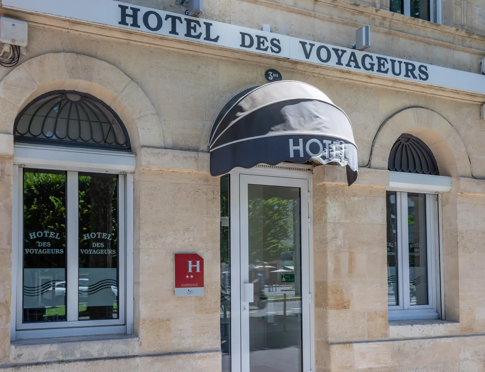 Facade of Hotel des Voyageurs in Bordeaux, a classic stone building featuring three arched windows, a central entrance door, and a black awning sign.