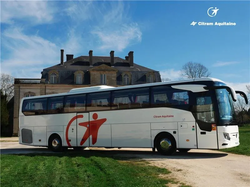 A white Citram Aquitaine bus parked in front of a historic castle in Bordeaux, displaying its distinctive red logo on the side of the vehicle.