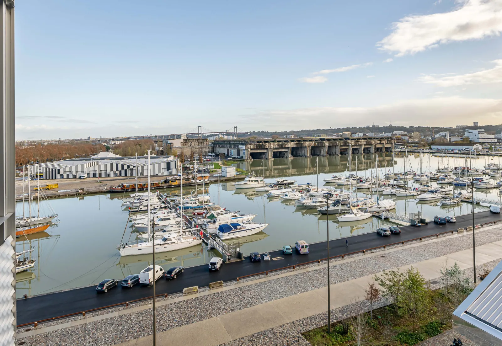 Panoramic view of Bordeaux's Bassins-à-Flot district featuring a marina full of sailboats, modern buildings and renovated historic warehouses along the waterfront.