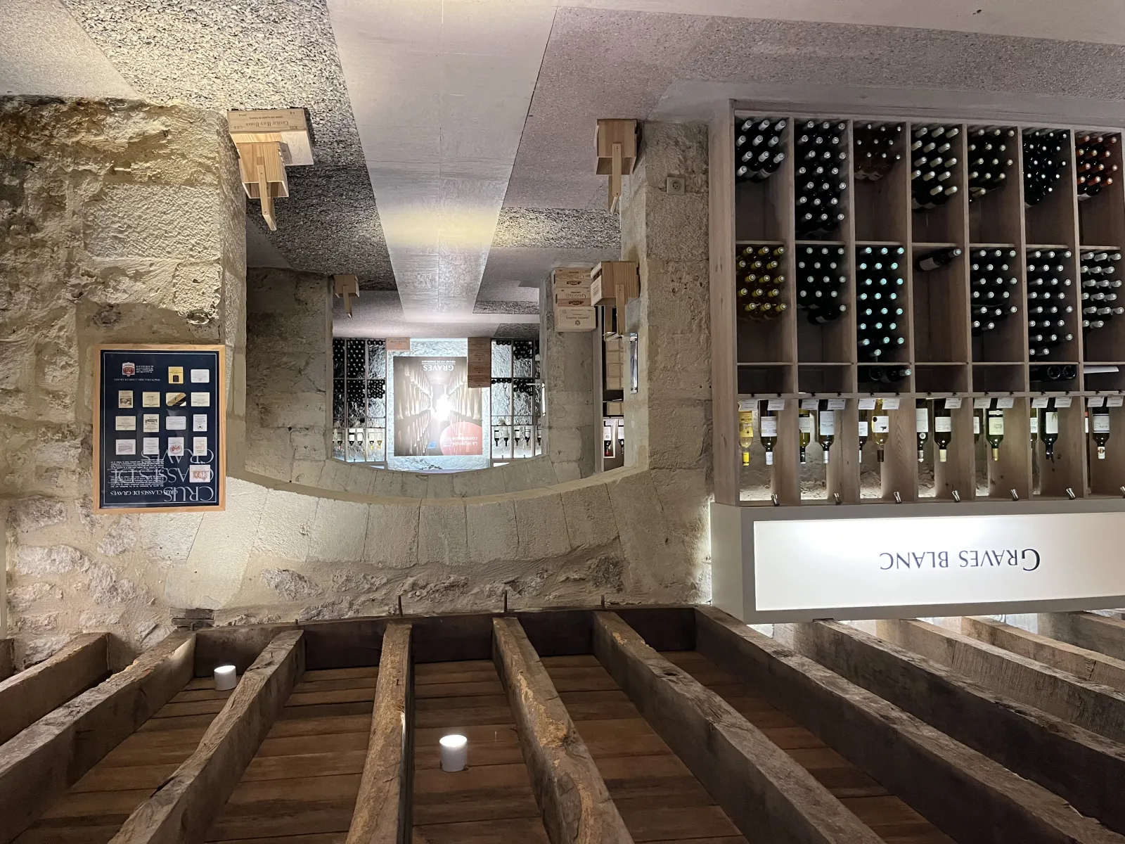 Interior of the Maison des Vins de Graves in Bordeaux, featuring wooden barrels, stone walls, wine bottle shelves, and informational displays.
