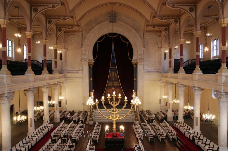 Interior of the Bordeaux Synagogue featuring a central nave, lateral galleries, ornamental columns, prayer benches, golden chandeliers and the golden ark above the altar