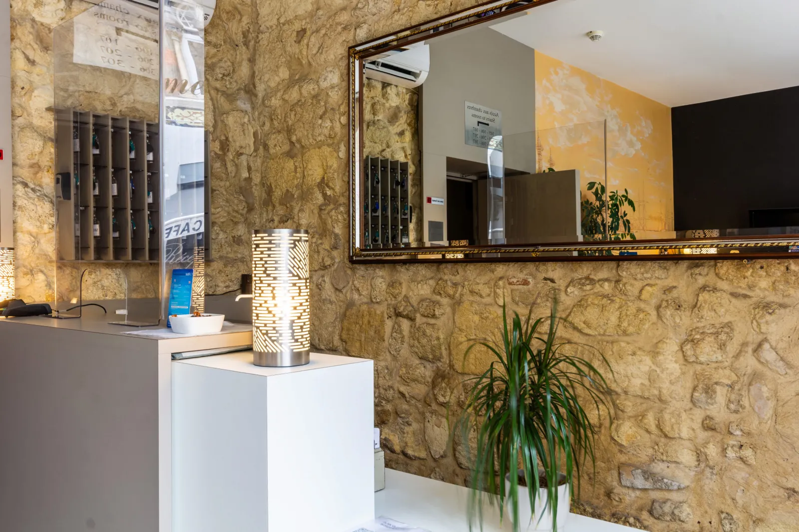 Elegant reception area of Hôtel Notre Dame in Bordeaux featuring golden stone walls, framed mirror, green plants and modern décor