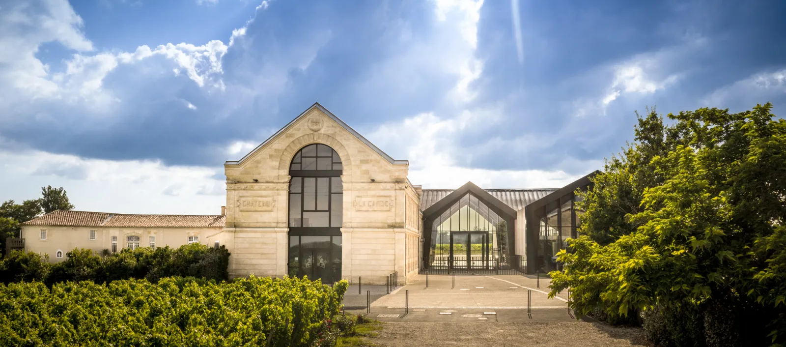 Château La Garde in Bordeaux featuring a stone facade with a distinctive arch and modern architectural extension with slate roofing, surrounded by lush vegetation.