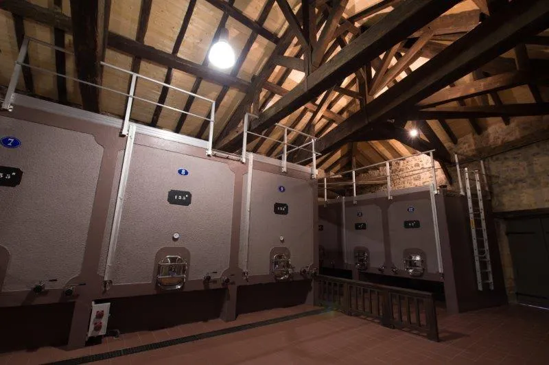 Interior of a winery with stainless steel fermentation tanks lined up under wooden beams, at Château de Portets in Bordeaux.
