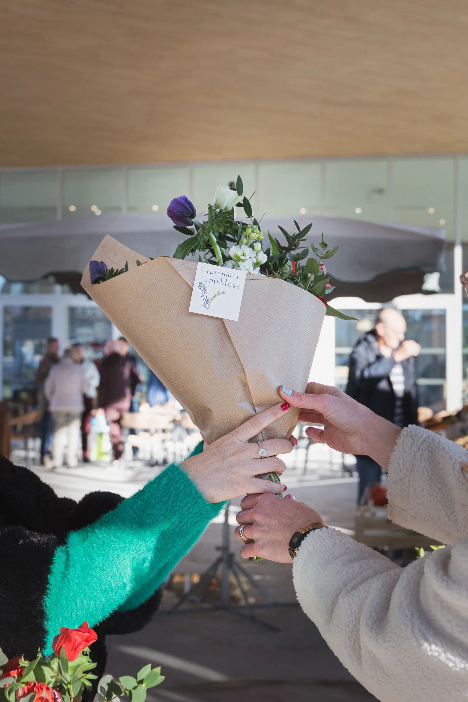 Two people exchanging a kraft paper-wrapped flower bouquet at the Vettiner Hall in Bouliac market in Bordeaux