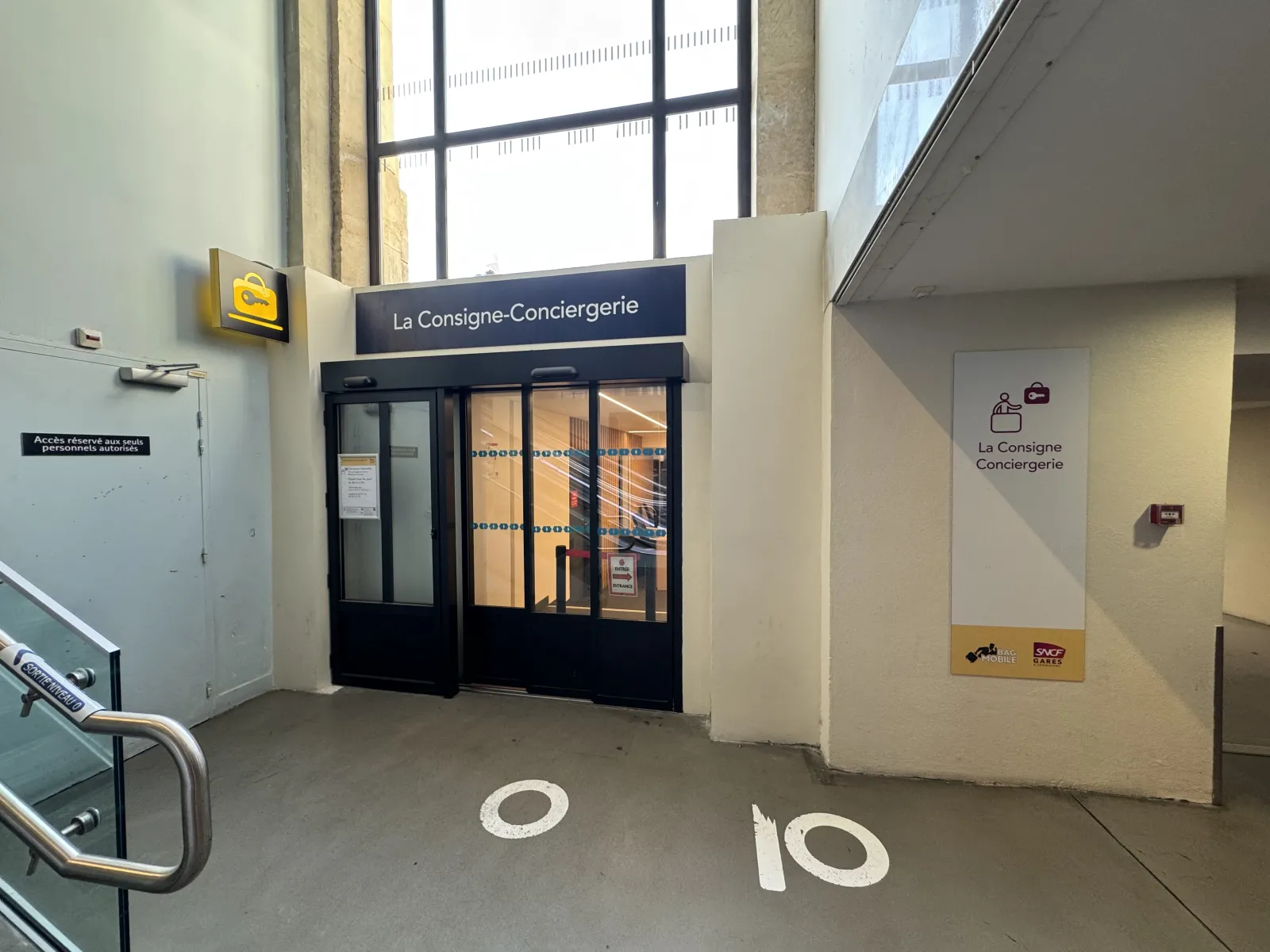 Storefront of La Consigne-Conciergerie, a luggage storage service in Bordeaux, featuring a black glass door, directional signage, and floor number 10 in a transit corridor.