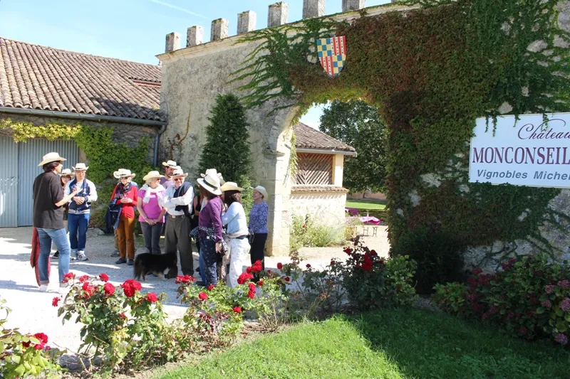 Group of visitors on a guided tour at Château Monconseil-Gazin in Bordeaux, gathered in the courtyard at the entrance decorated with red flowers and vines.