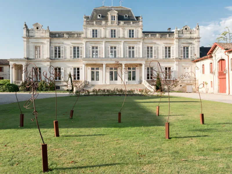 Main facade of Château Giscours in Bordeaux, an imposing white Second Empire mansion with mansard roofs, surrounded by a lawn featuring modern metal sculptures.