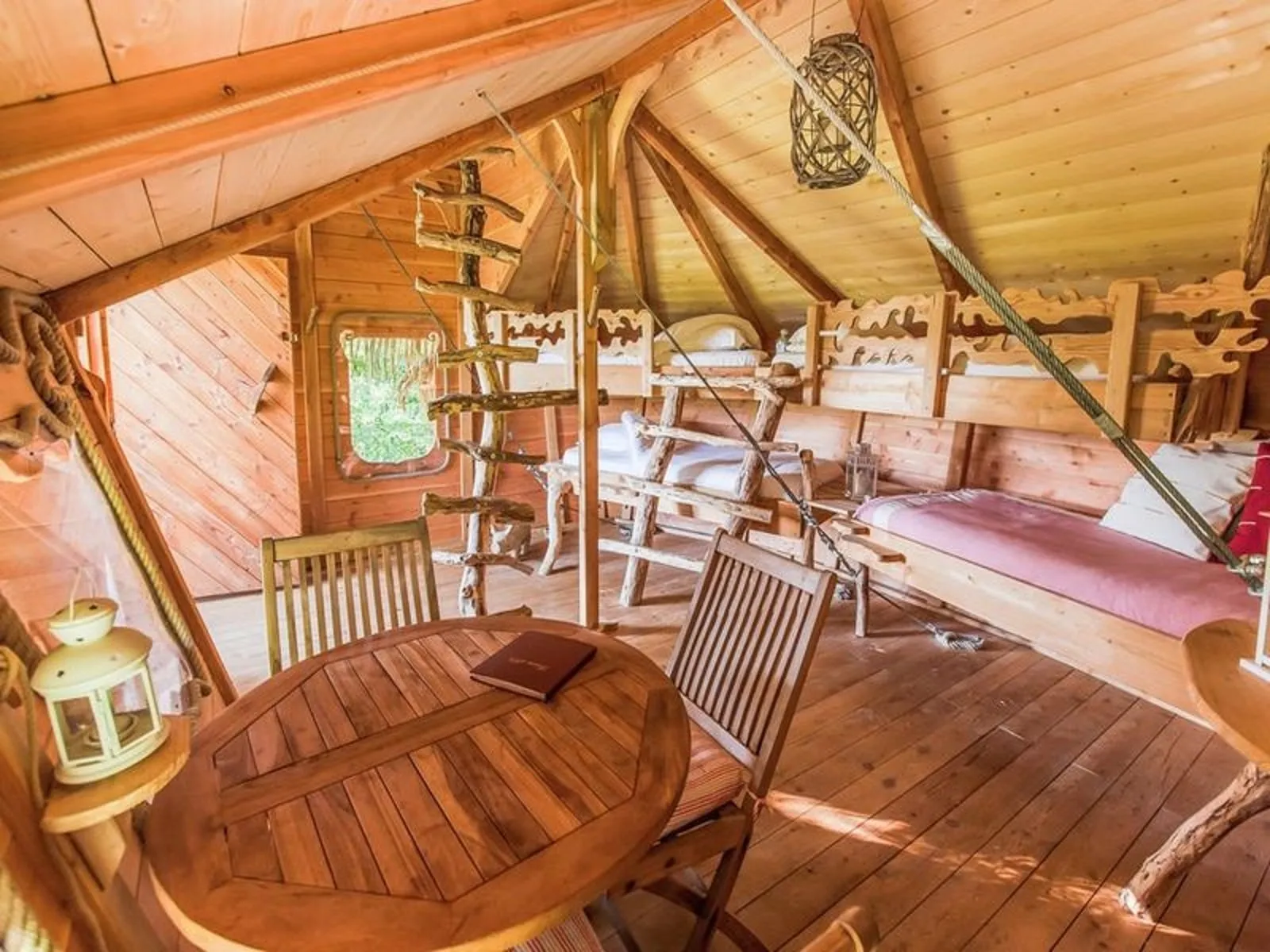 Spacious wooden cabin interior with rustic furniture, bunk beds, round table and chairs, panoramic window overlooking nature at Les Cabanes de la Romaningue in Bordeaux