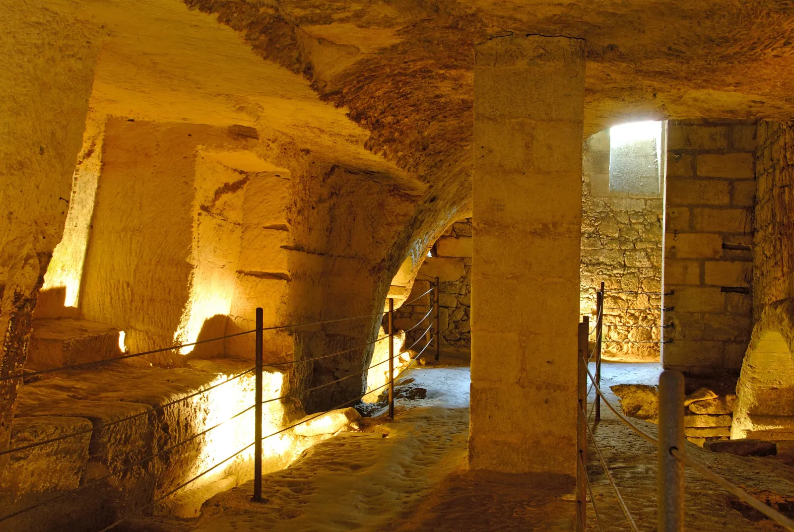 Vaulted underground gallery in Saint-Emilion with stone columns, warm lighting and metal stairs