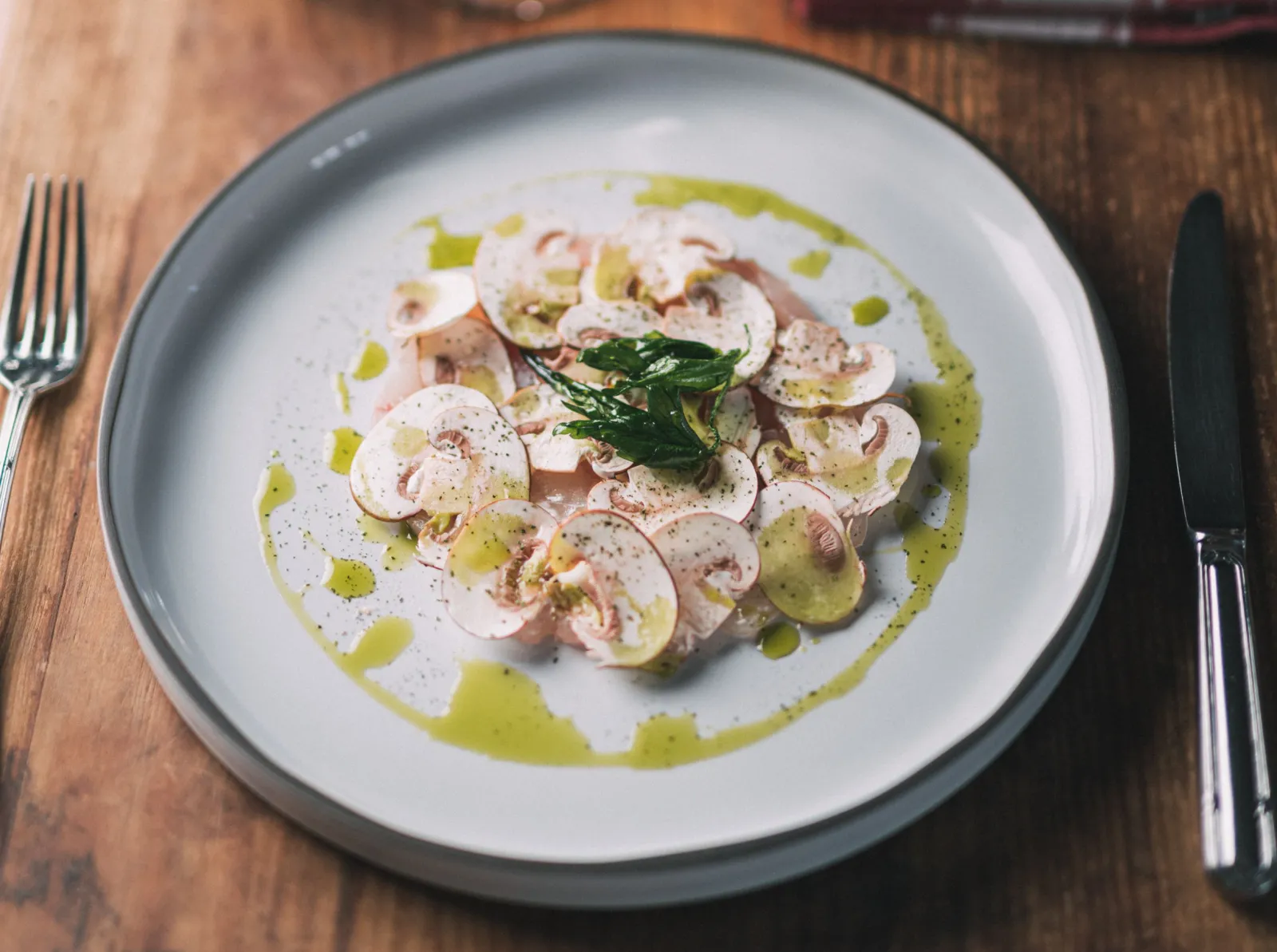 Refined seafood dish featuring sliced scallops, mushrooms, and green sauce with fresh herbs and pepper, presented at La Table du Lavoir in Bordeaux