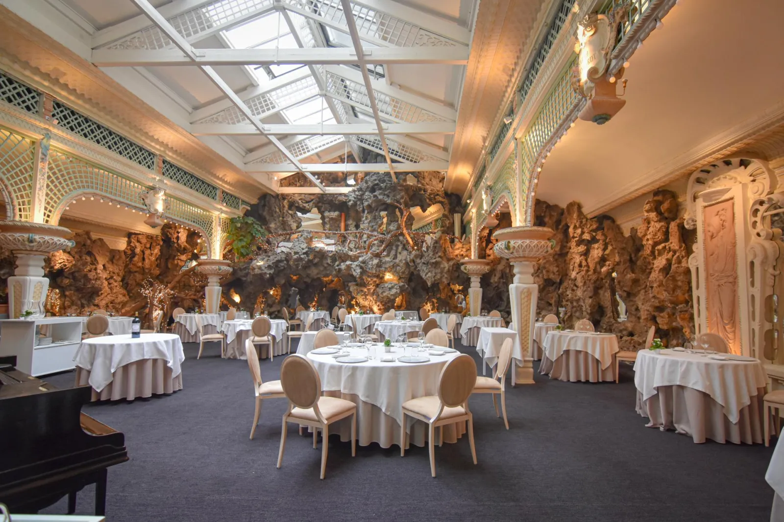 Elegant banquet hall at Chapon Fin in Bordeaux featuring round tables with white tablecloths, ornate golden stone decor, decorative columns, and a glass ceiling.