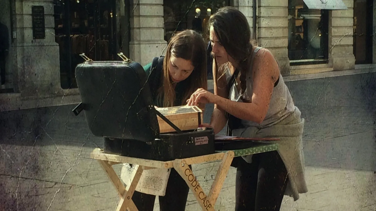 Two women examine a document next to a street bin on the cobbled streets of Bordeaux in the rain.