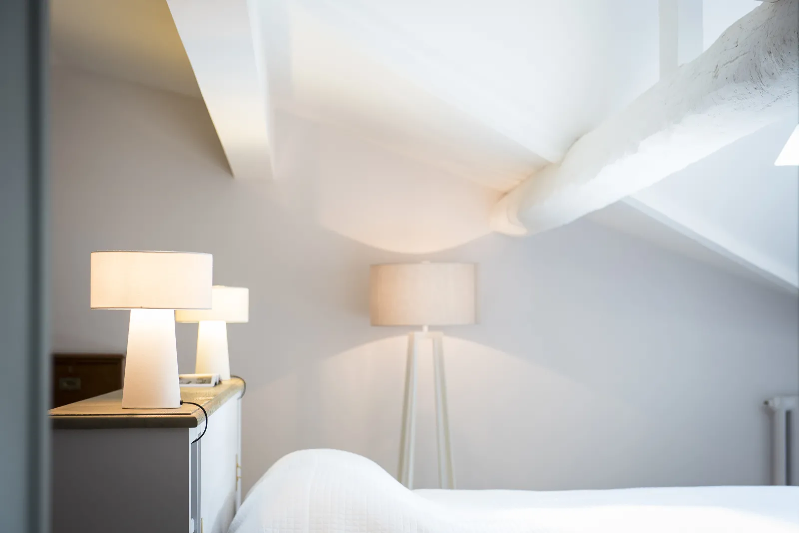 Elegant bedroom with two illuminated table lamps, white ceiling with exposed beams, and minimalist furnishings at La Chartreuse Haut-Bailly in Bordeaux.