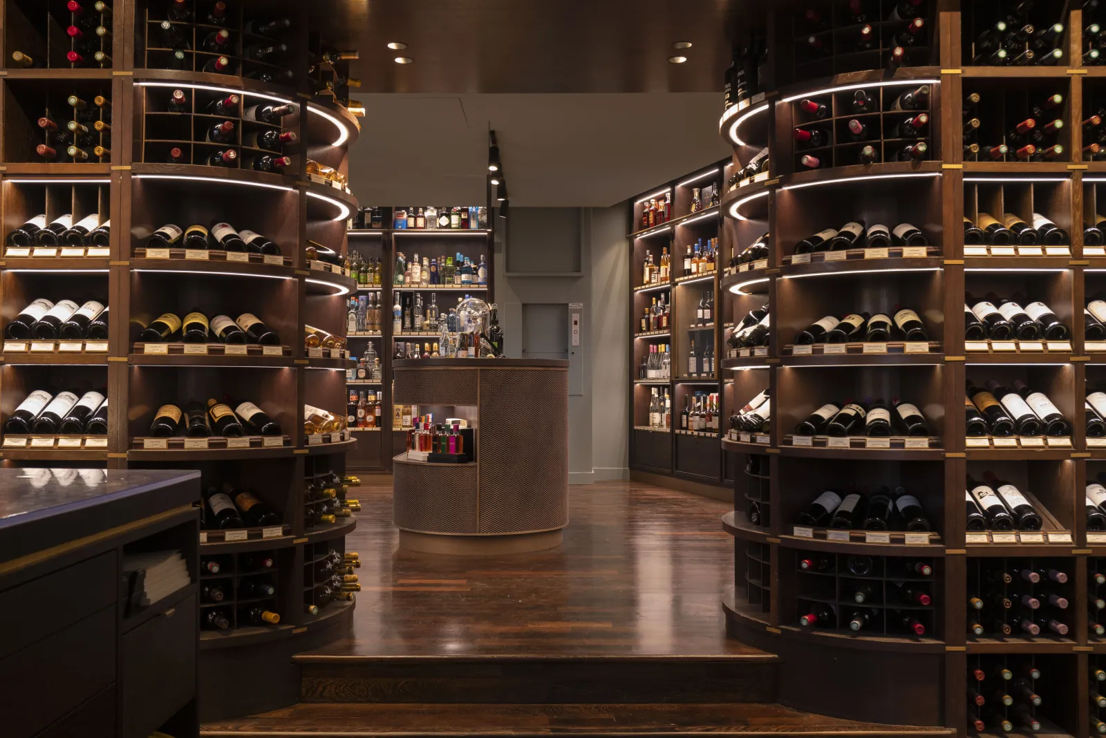 Elegant wine cellar interior featuring curved wooden shelves displaying red and white wine bottles, illuminated by white neon lighting, in the heart of Bordeaux.
