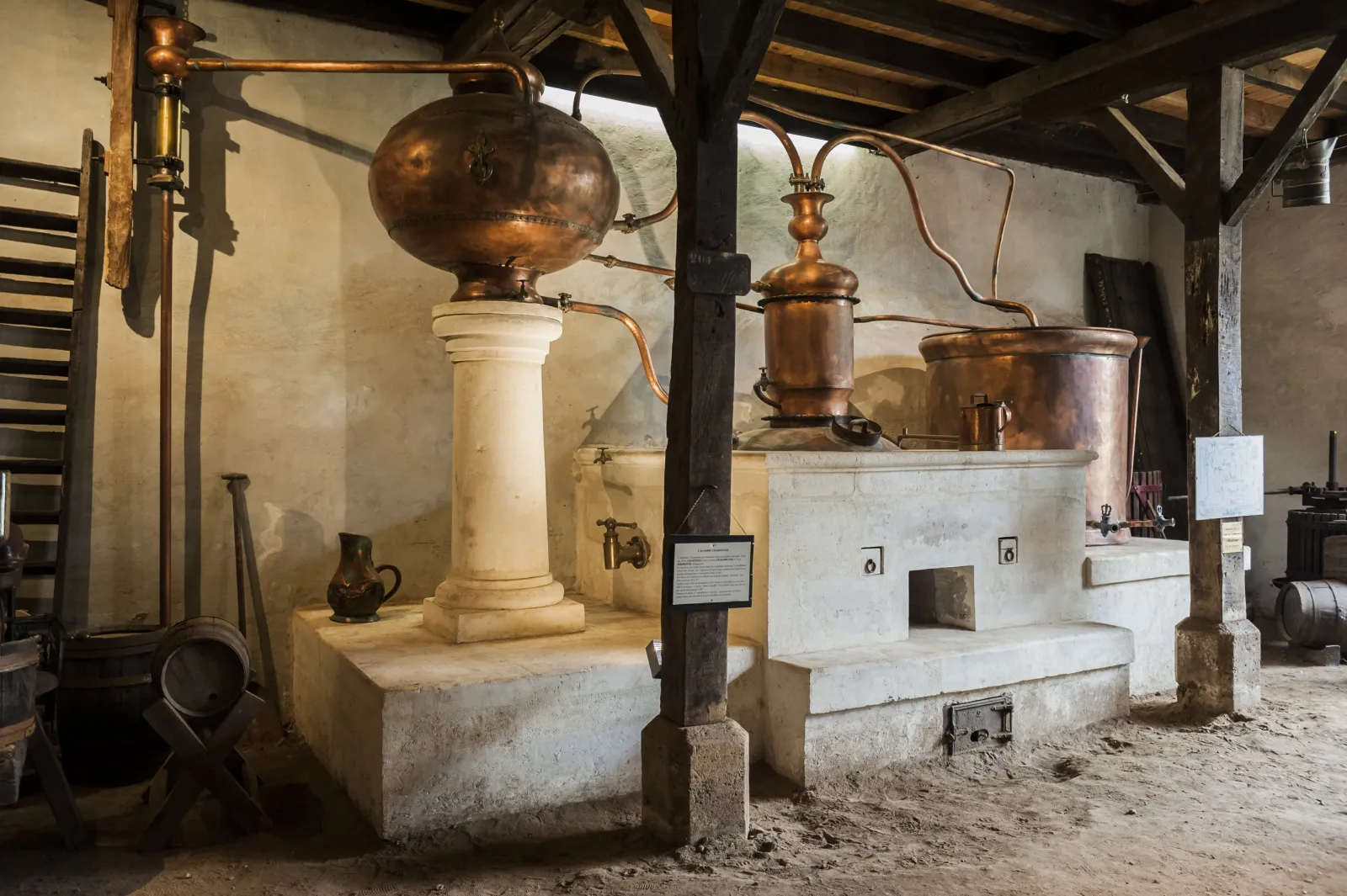 Interior of a wine museum displaying traditional copper stills and distillation equipment on stone platforms, with aged walls and exposed wooden beams.