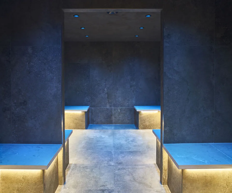 Modern underground swimming pool at La Zoologie spa in Bordeaux featuring blue and gold lighting, slate textured walls and staircase access