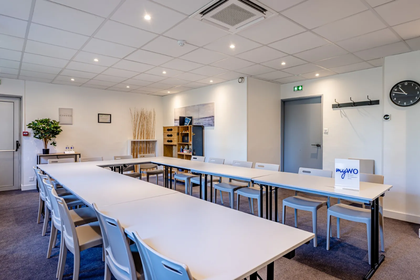 Modern meeting room at Sure Hotel by Best Western Bordeaux Lac featuring white modular tables, blue chairs, suspended ceiling, LED lighting, and audiovisual equipment.