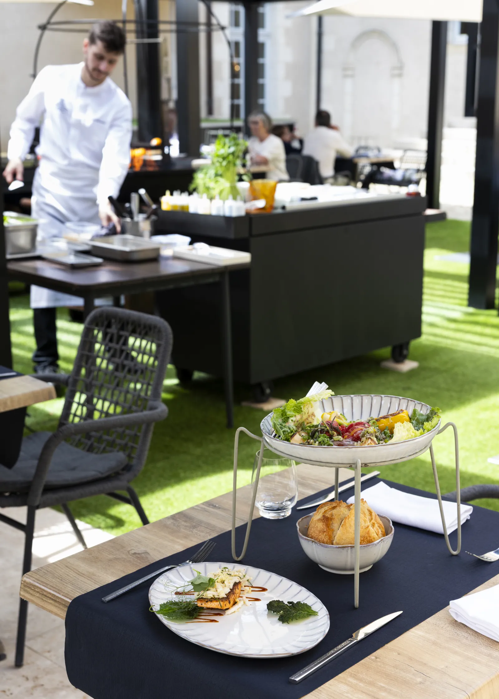 Restaurant terrace with set tables, gourmet dishes and kitchen staff, on synthetic grass background in Bordeaux
