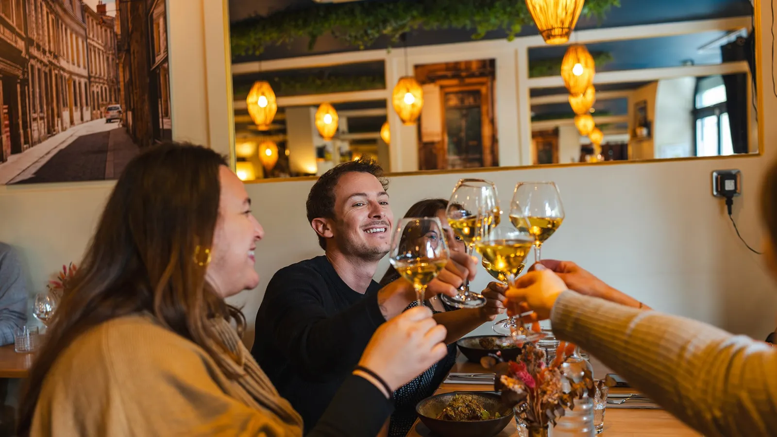 A group of people toast with glasses of white wine in an elegant Bordeaux restaurant during a gourmet food tour.
