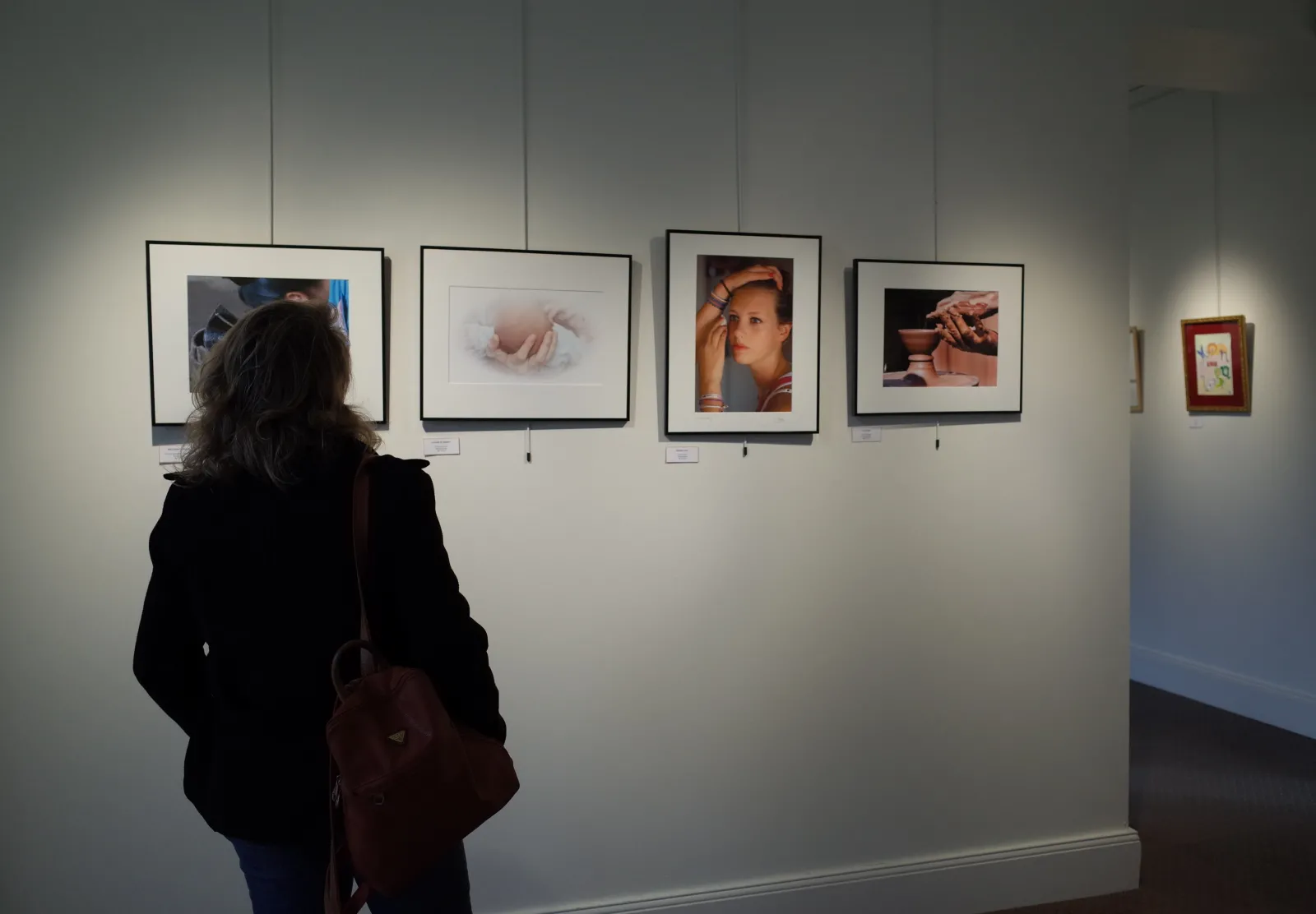 A visitor examines framed photographs displayed on a white wall at the Georges de Sonneville Museum in Bordeaux, featuring portraits and artistic studies in black and white and color.