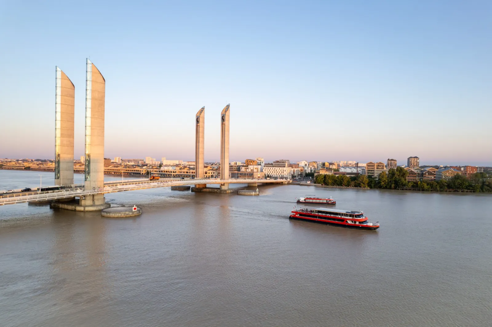 The Lifting Bridge of Pierre d'Espagne in Bordeaux with two red tourist boats navigating the Garonne River at sunset