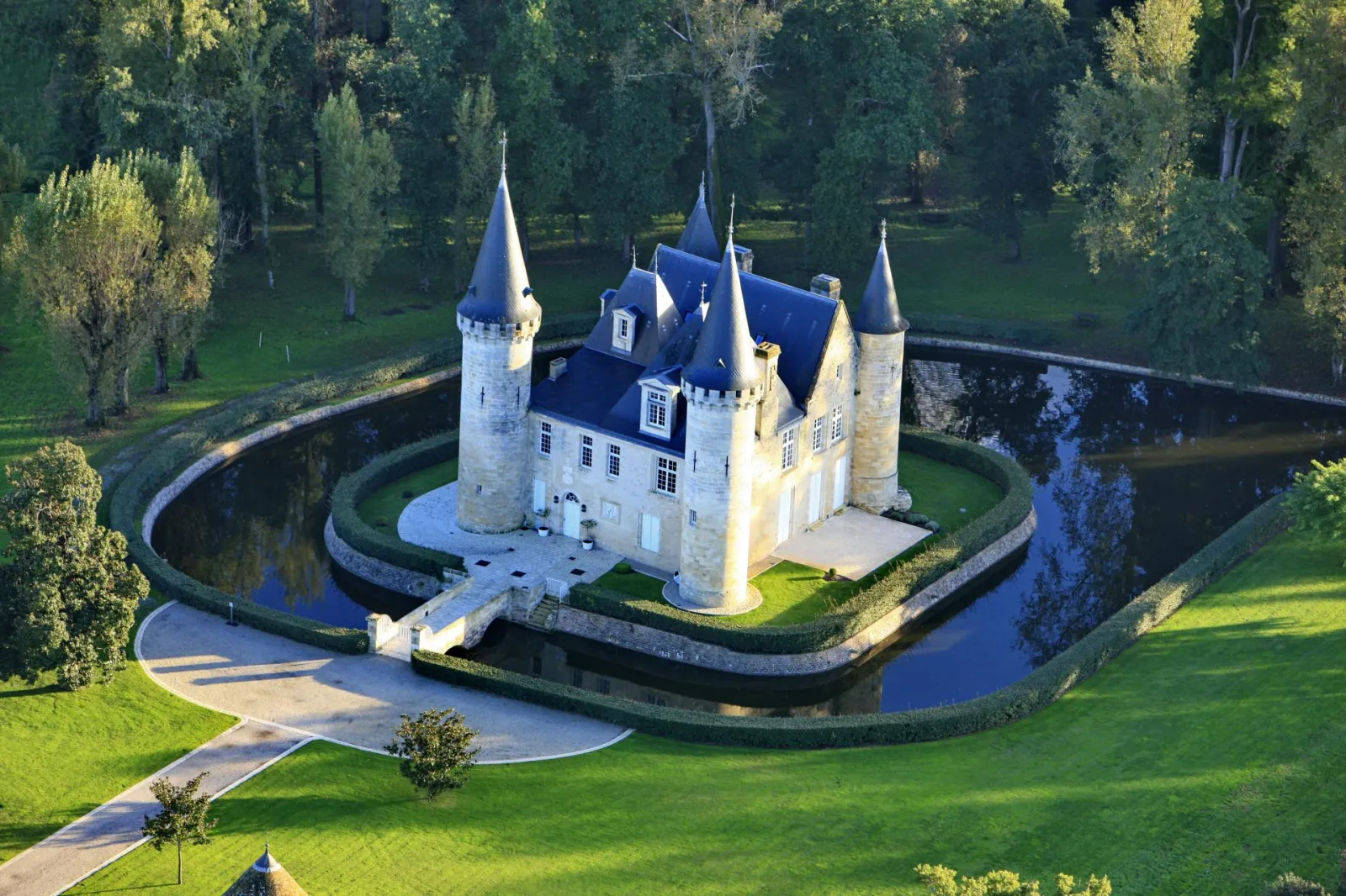 Aerial view of Château d'Agassac near Bordeaux, a medieval fortress with pointed towers surrounded by a water moat and lush greenery