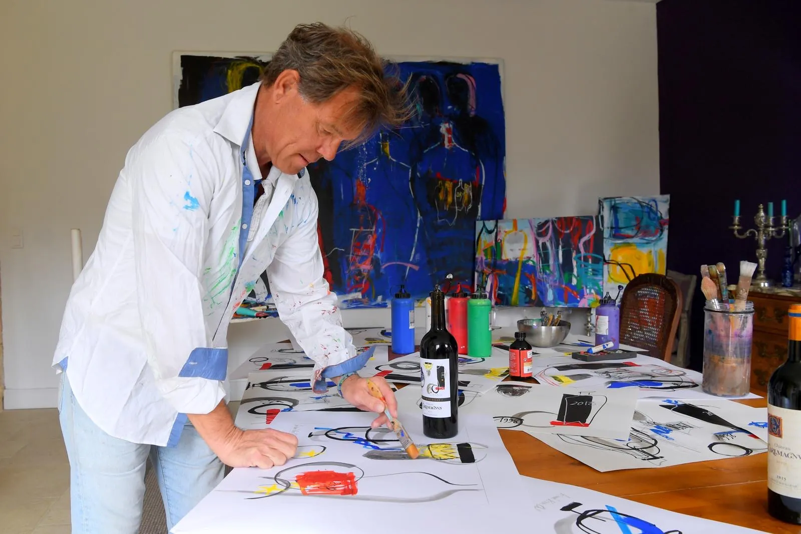 An artist painting in the studio at Château CarlMagnus in Bordeaux, surrounded by colorful abstract artworks and artistic supplies.