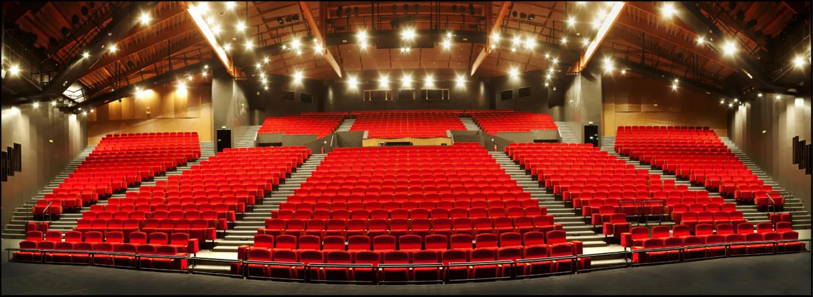 Modern cinema auditorium with hundreds of red seats arranged in rows, ceiling lighting, at Bordeaux Le Pin Galant.