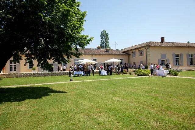 The Cadillac Wine House featuring its ochre-yellow facade, expansive green lawns, and visitors gathering for an outdoor event under a white tent.