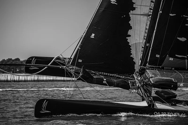 Black sailing yacht with deployed sails on water in Bordeaux, detailed view of rigging and boat structure in black and white.