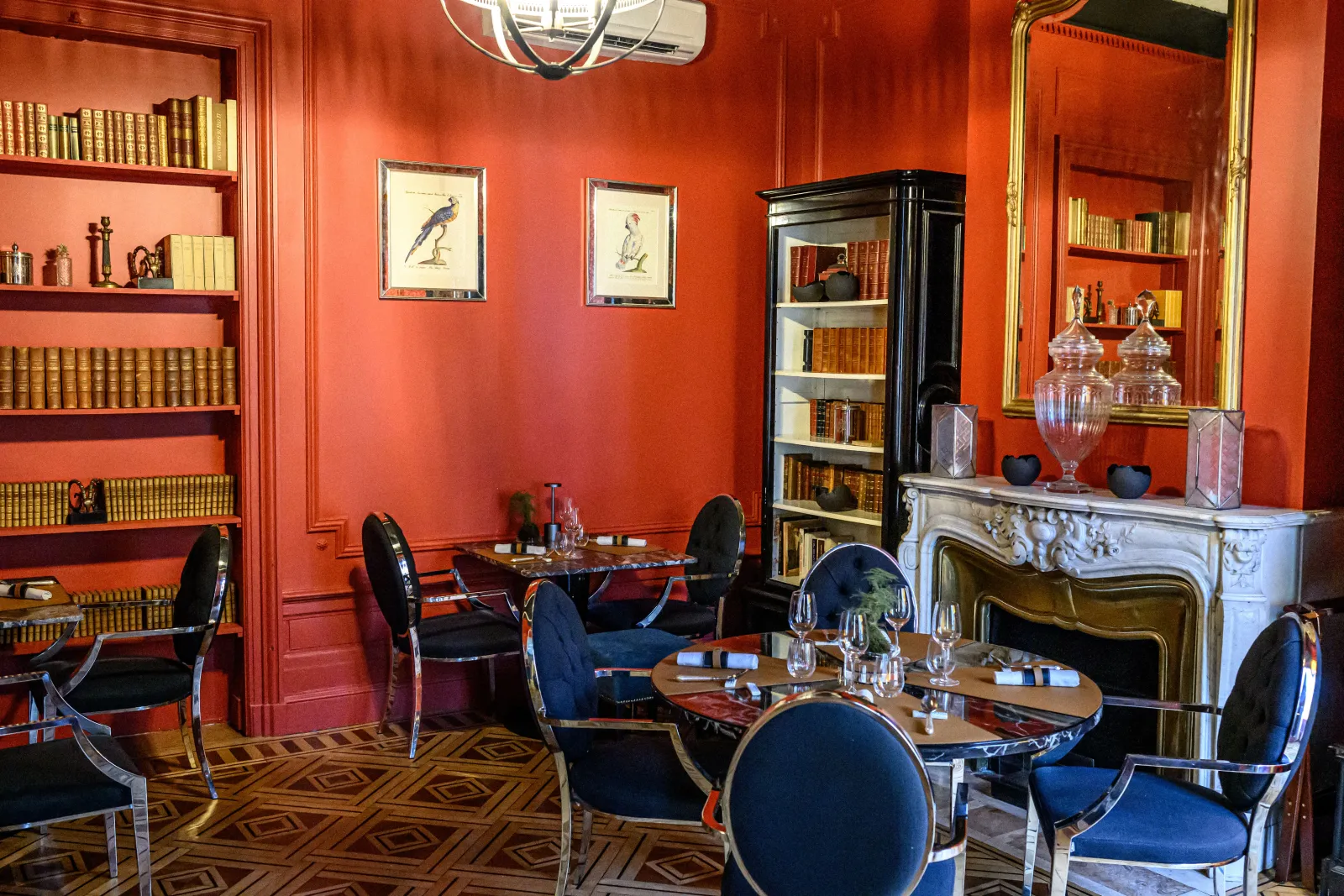 Elegant interior of the Cercle de Montaigne in Bordeaux featuring red walls, blue and gold furniture, book-lined shelves, white fireplace, and dining tables.