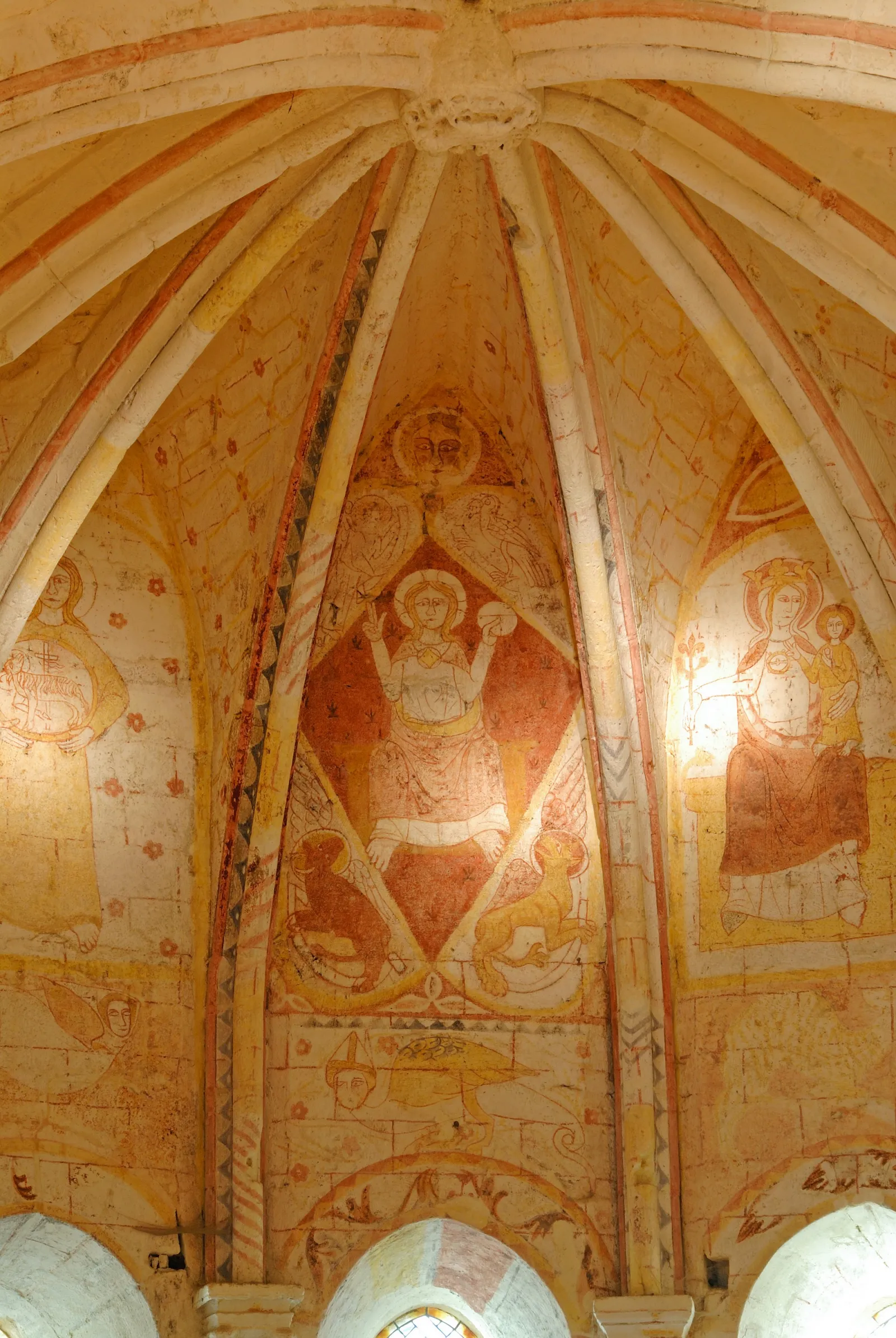 Underground medieval chapel interior with barrel vault ceiling, ochre-colored frescoes depicting religious figures, and radiating columns in Saint-Emilion.