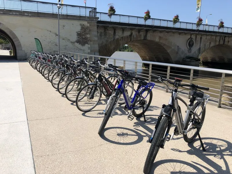 Lovelec bike-sharing station in Bordeaux with multiple bicycles lined up under a stone bridge overlooking the Garonne river
