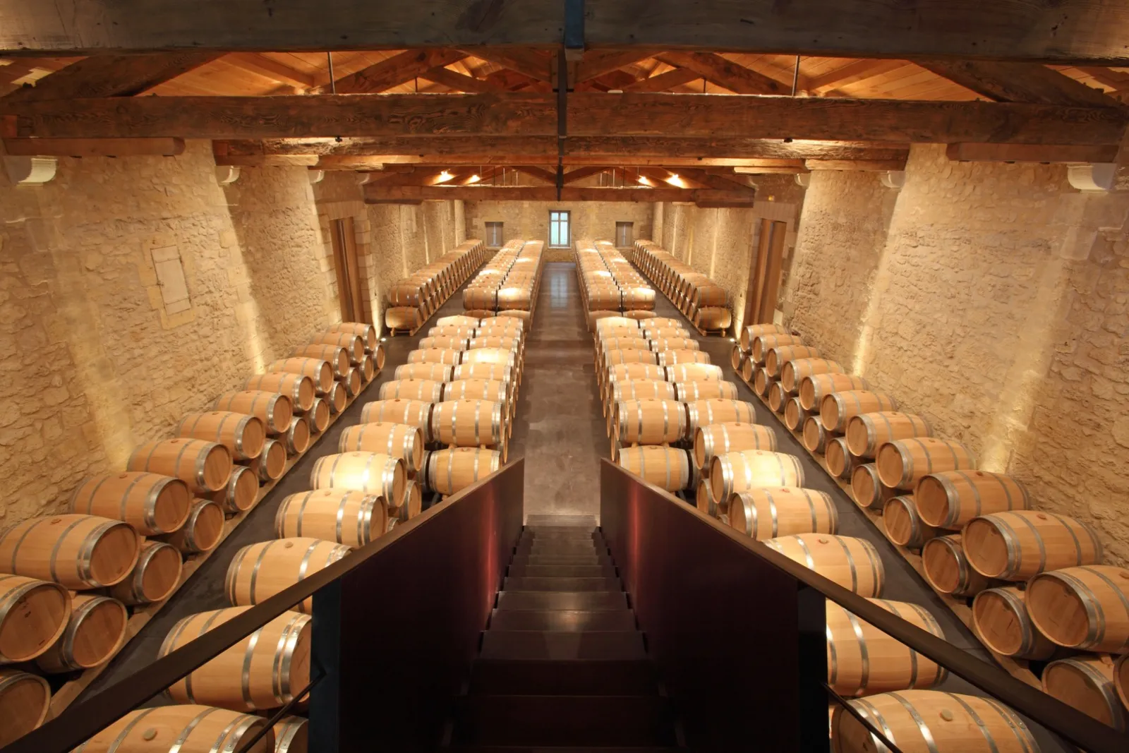 Interior of a wine cellar featuring symmetrically arranged wooden oak barrels under exposed wooden beams at Château de Ferrand in Bordeaux.