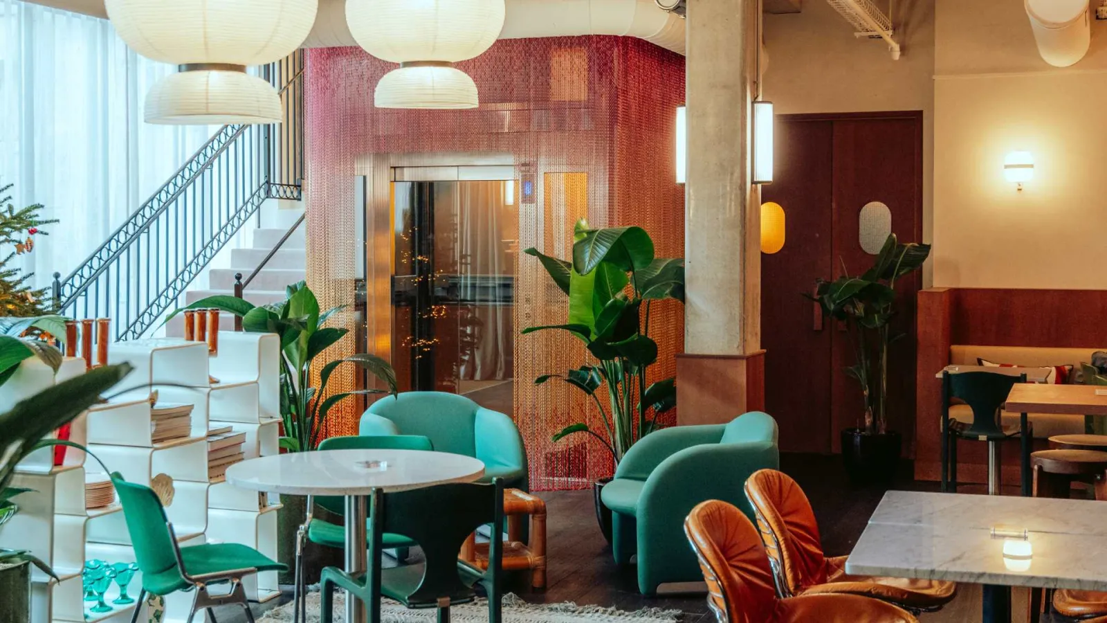 Modern hotel interior in Bordeaux featuring mint green furniture, indoor plants, designer lighting, metal staircase, and orange and red decorative accents.
