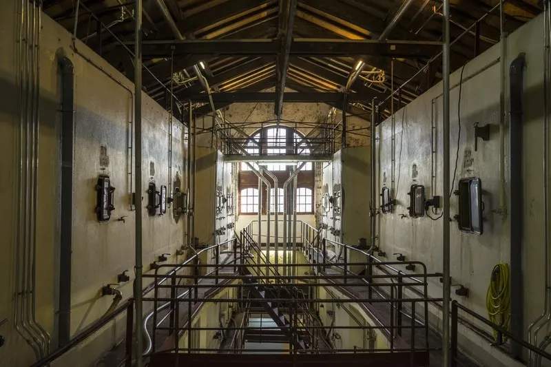 Interior of a wine cellar featuring metal cellar doors lined on both sides of a central corridor, with exposed metal framework and scaffolding visible, at Cave La Rose Pauillac in Bordeaux.
