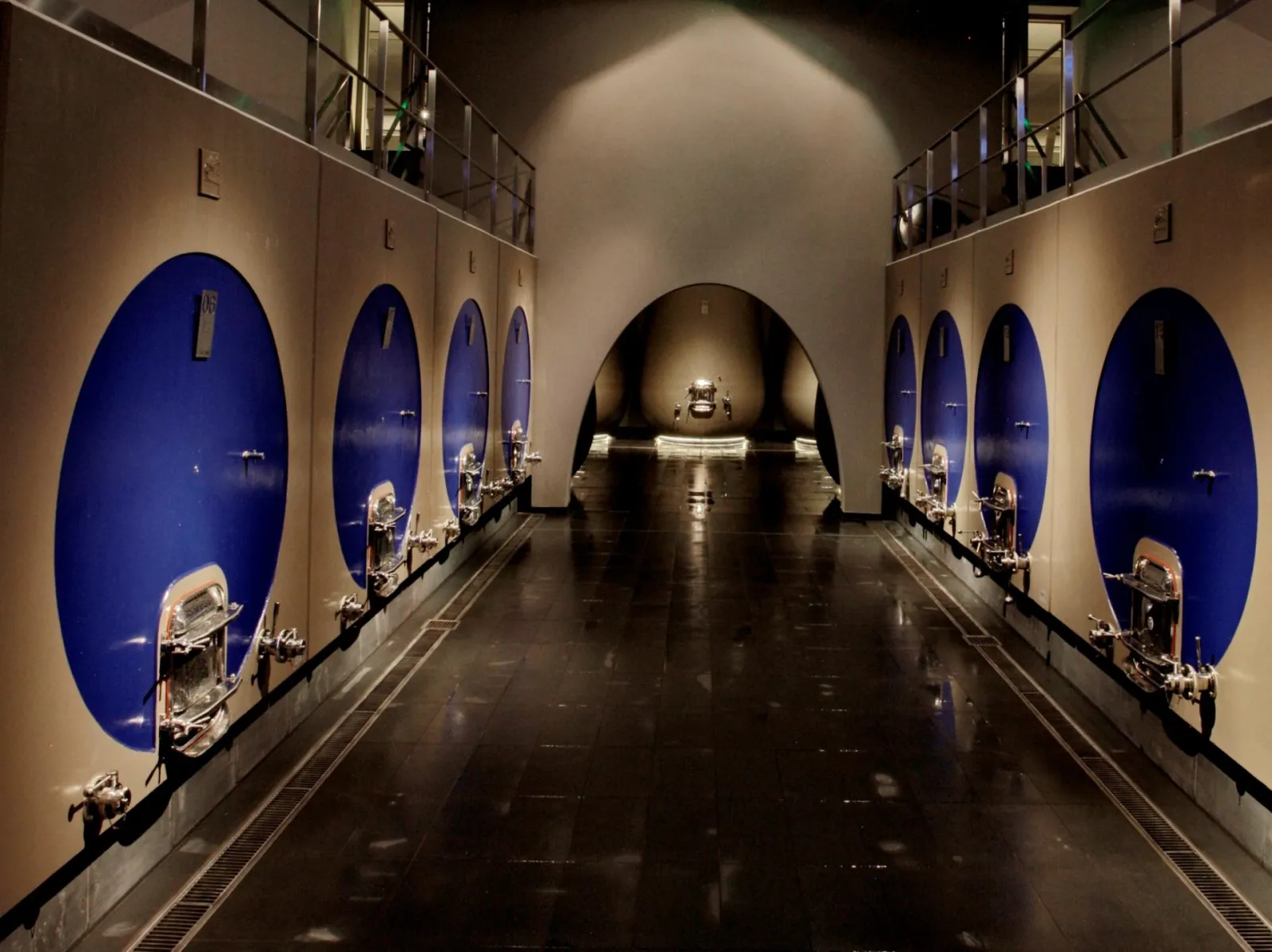 Underground cellar gallery at Château Prieuré-Lichine in Bordeaux featuring wine barrels displayed in illuminated blue niches along the walls with a central arched vault.