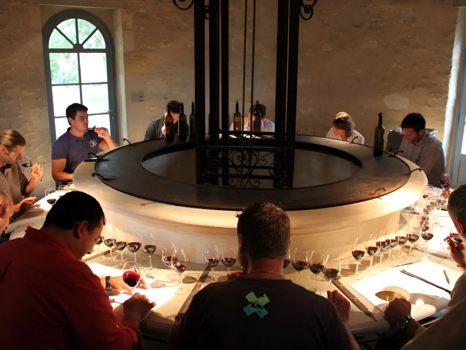 Wine tasting around a circular table at Château de Reignac in Bordeaux, with red wine glasses arranged in rows and visitors seated around the table.