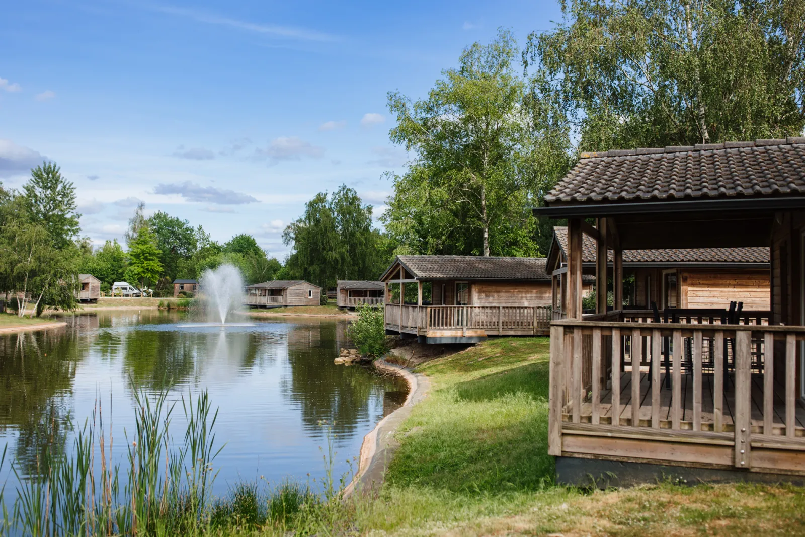 Holiday village with wooden cabins along a lake, central fountain, trees and blue sky, Yelloh! Village Bordeaux Lac