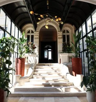 Elegant entrance to Grand Barrail restaurant in Bordeaux featuring a covered gallery with stone arches, green plants, and black doors