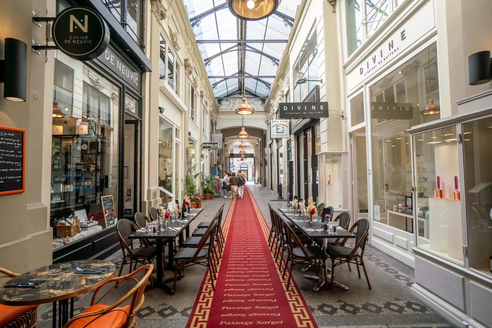 Elegant covered arcade in Bordeaux with luxury shops, restaurant tables, glass ceiling and red carpet on the floor
