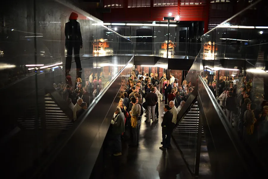 Interior view of Rocher de Palmer in Cenon showing a crowd of visitors in a modern corridor with stairs, contemporary lighting, and exhibition displays.