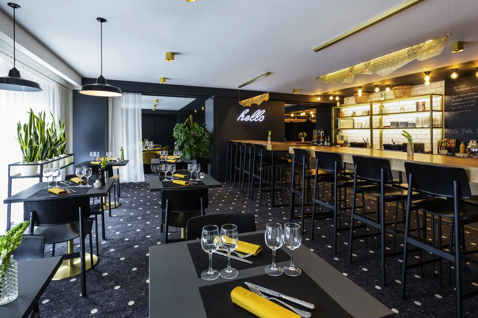 Elegant restaurant at Mercure Bordeaux Centre hotel featuring black and gold table settings, illuminated bar counter, blue 'hello' neon sign, and contemporary décor with plants.