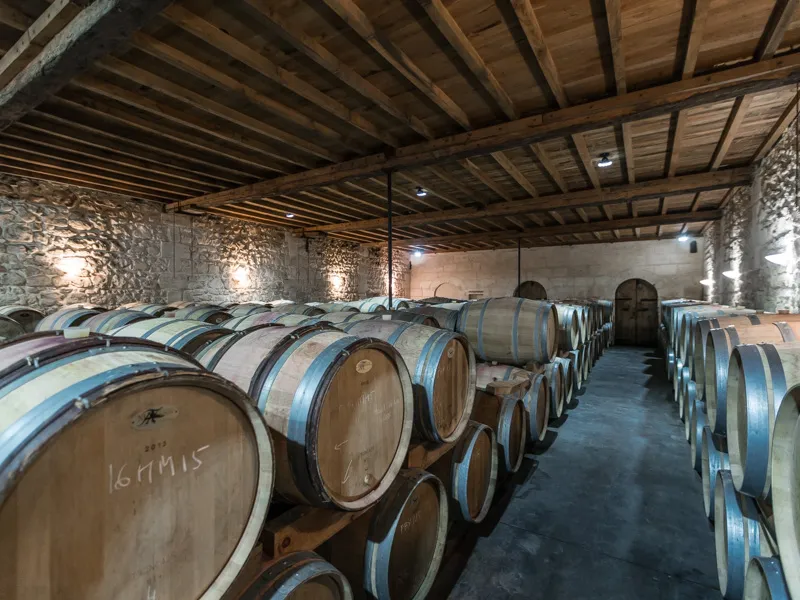 Wine aging cellar with rows of blue and white oak barrels in a stone building with exposed wooden beams, Château Beau Rivage, Bordeaux