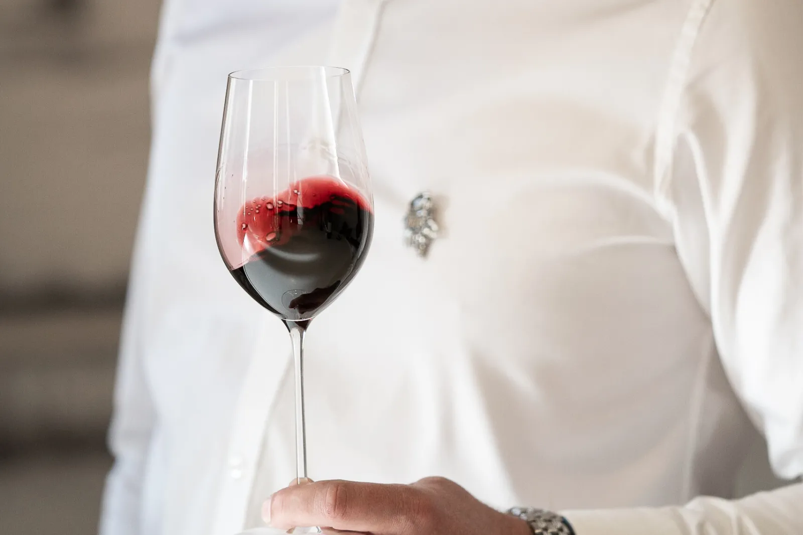 A person in white clothing holds a glass of red wine at Bordeaux, Château de Ferrand