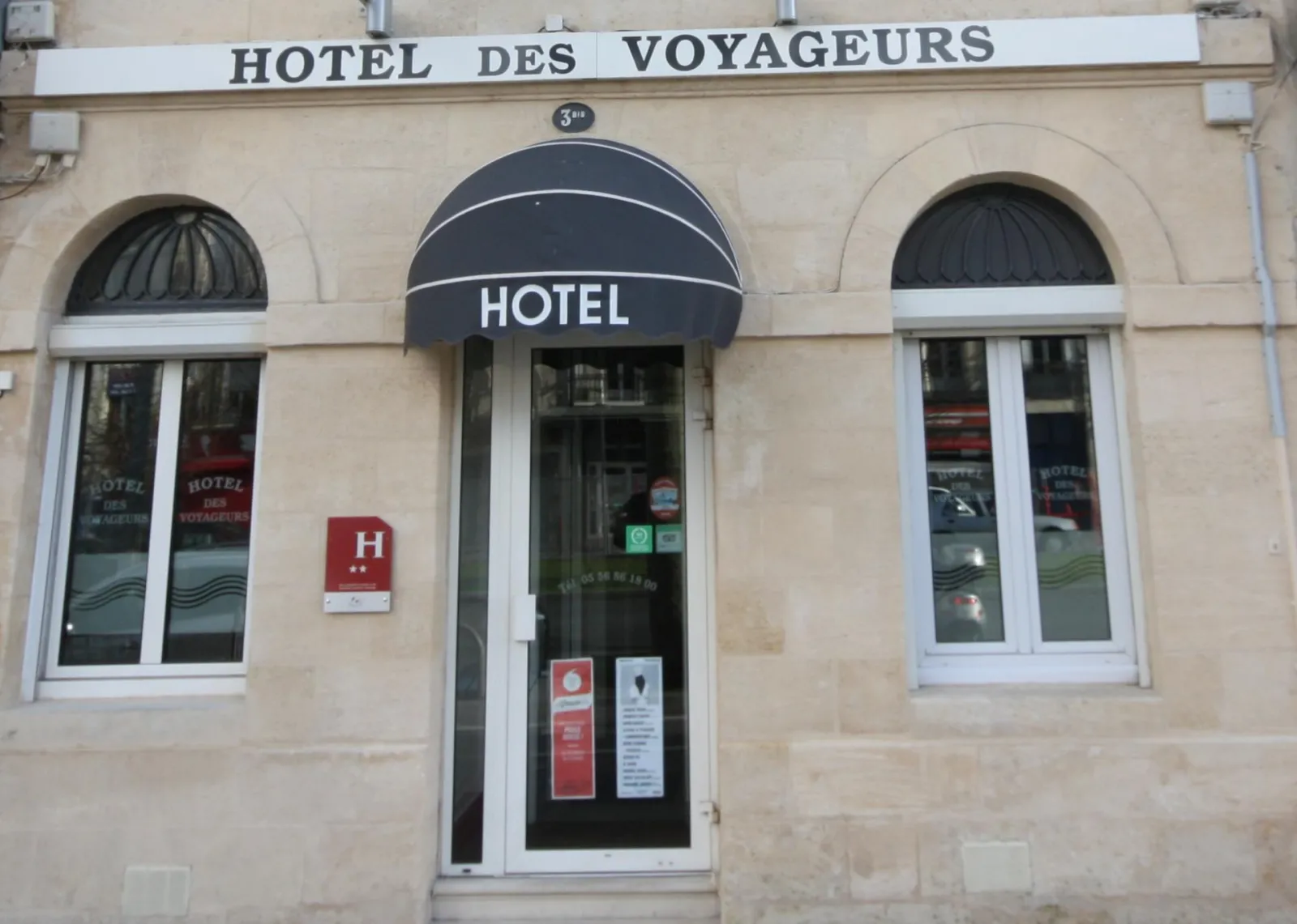 Facade of the Hotel des Voyageurs in Bordeaux, a beige stone building with three arched windows, central entrance under a dark blue awning and hotel signage.