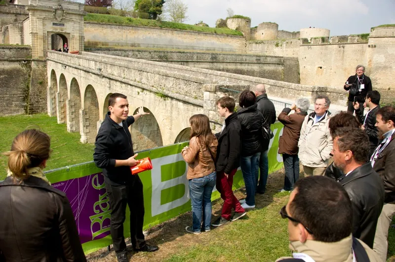 A group of visitors during a guided tour of Blaye Citadel, listening to a guide standing in front of a stone bridge crossing the fortress moat.