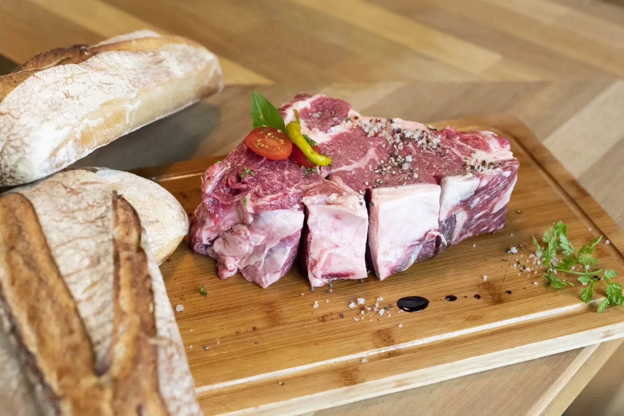 Charcuterie board with sliced raw meat, artisanal bread, fresh herbs and garnish displayed on a wooden cutting board